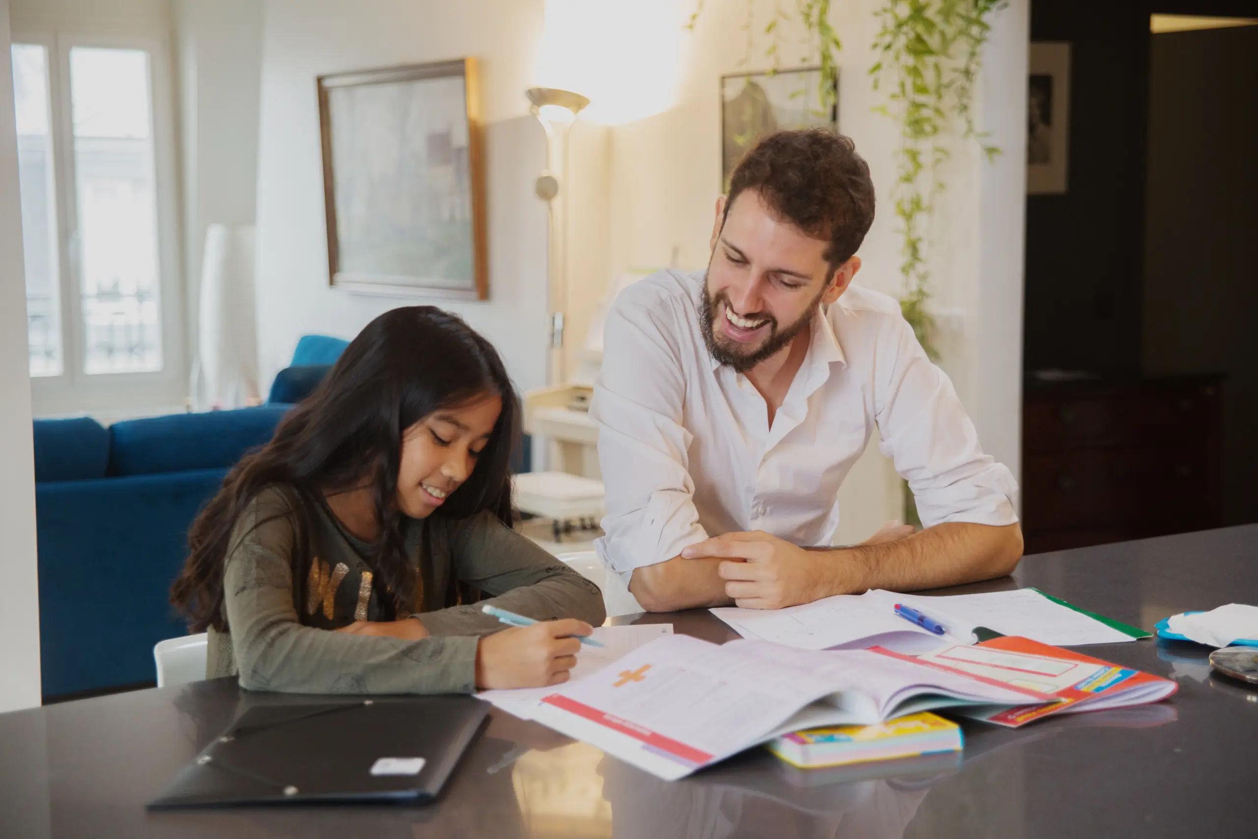 man sitting at a table with a student who is working in a notebook