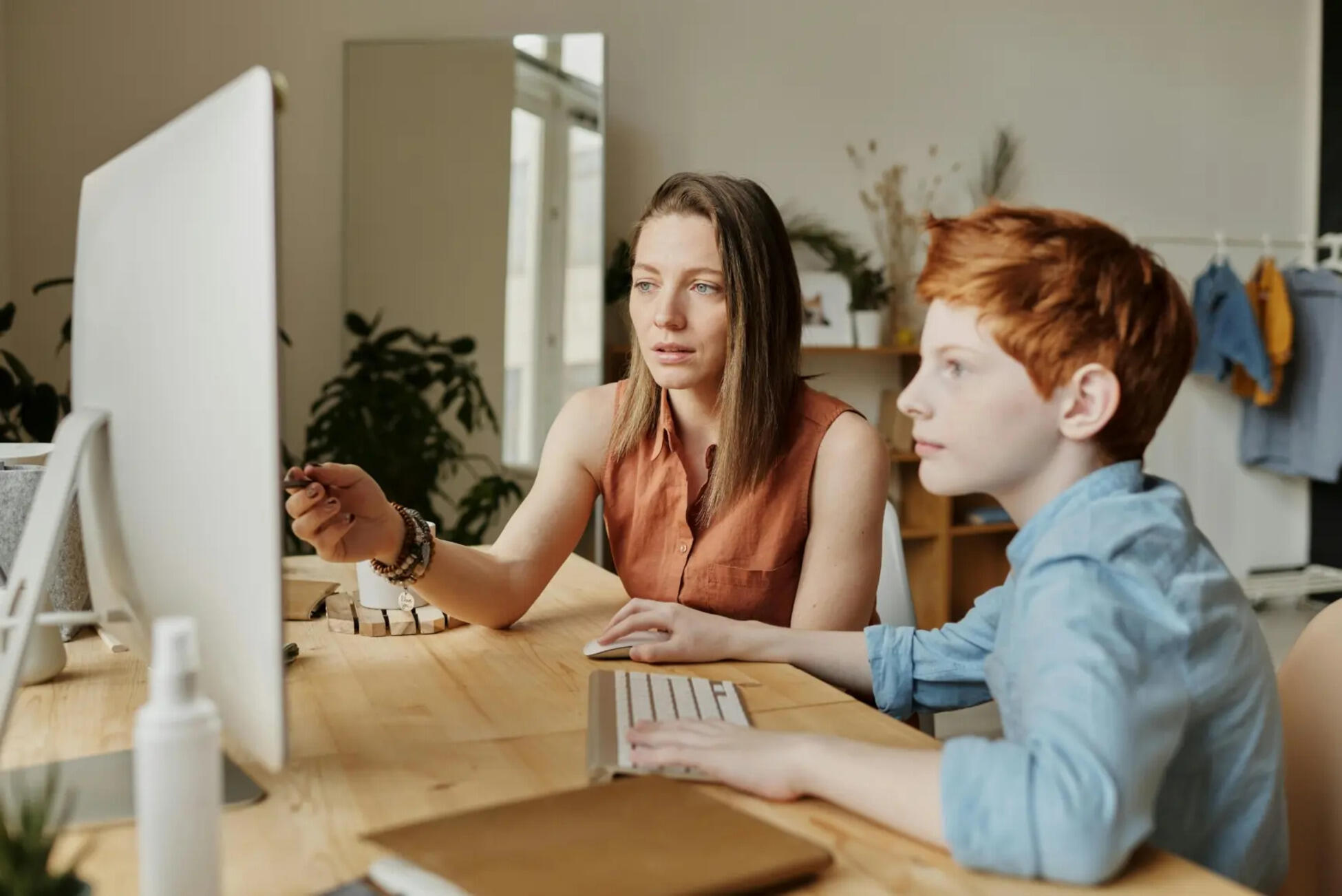 a woman and a young boy sitting at a desk looking at a computer screen